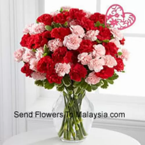 36 Oeillets (18 rouges et 18 roses) avec des remplissages saisonniers et un bâton de cœur de la Saint-Valentin dans un vase en verre